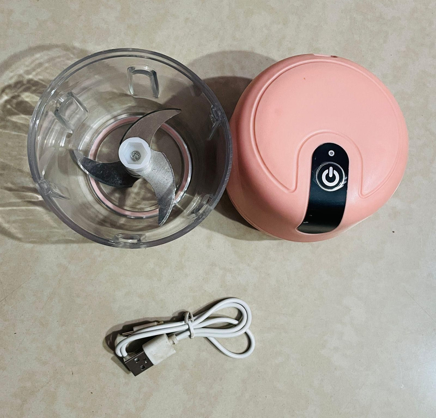 Pink handheld blender with clear container and power cord on a beige surface